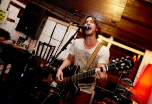 Mentor and Vocal Coach Ben Hellings singing on a mic playing guitar.