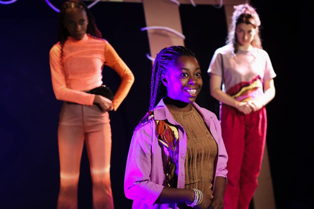 Young girl stood on stage with two others stood behind her one on either side.