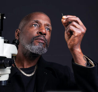 Dr Willard Wigan looking at his sculpture next to a microscope.