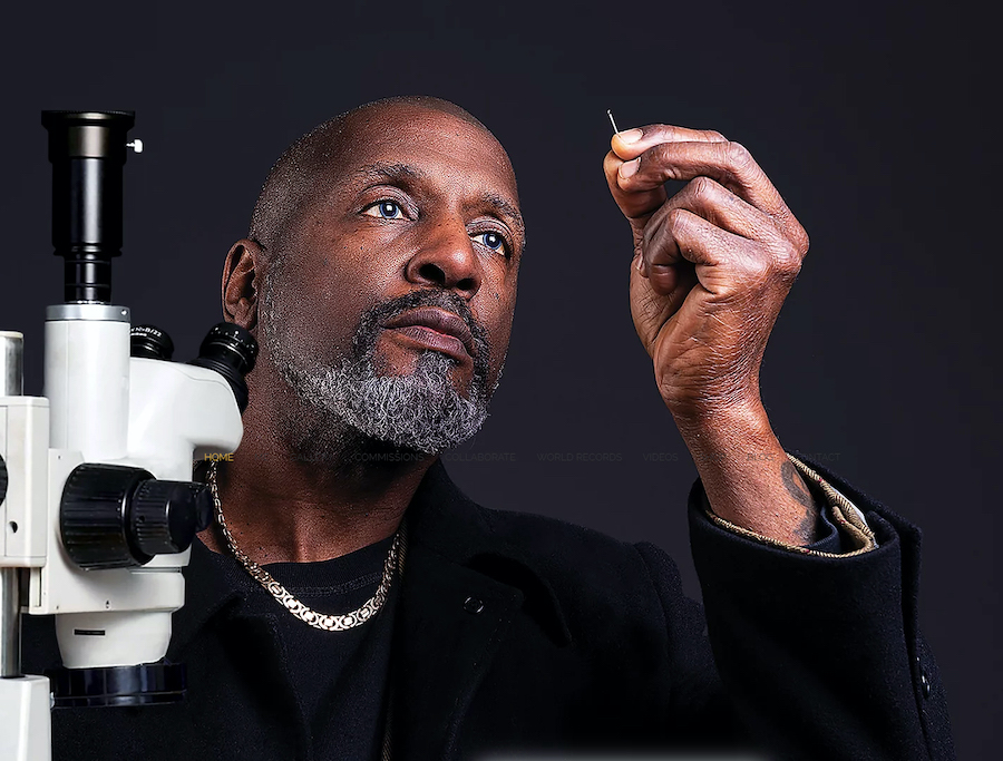 Dr Willard Wigan looking at his sculpture next to a microscope.