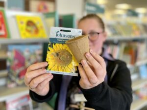 Lady holding a pack of seeds towards the camera which are in focus.