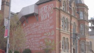 An exterior building wall with a poem written on it in Nottingham. The poem is called here and now.