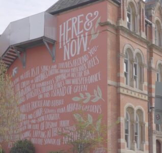 An exterior building wall with a poem written on it in Nottingham. The poem is called here and now.