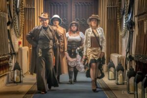4 people in a hallway, waling towards the camera dressed in steampunk clothing.