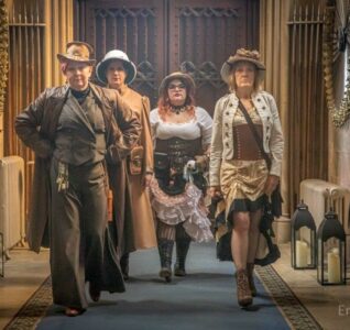4 people in a hallway, waling towards the camera dressed in steampunk clothing.