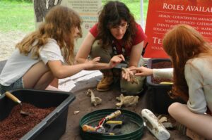 An Archaeologist excavating something at Creswell Crags with two young girls.
