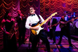 Buddy Christopher on stage in a white shirt and bow tie with a fender guitar