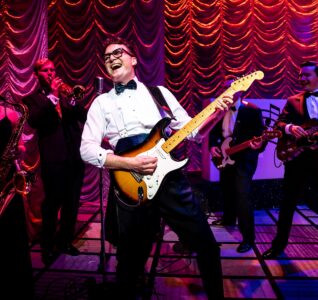 Buddy Christopher on stage in a white shirt and bow tie with a fender guitar