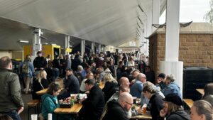 People at a street food festival under a cover eating together on benches.