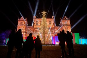 A family with their back to camera, looking on at Wollaton Hall and Tree which is all lit up for Christmas at Wollaton.