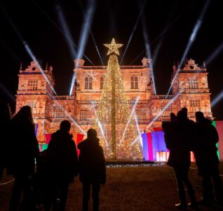 A family with their back to camera, looking on at Wollaton Hall and Tree which is all lit up for Christmas at Wollaton.