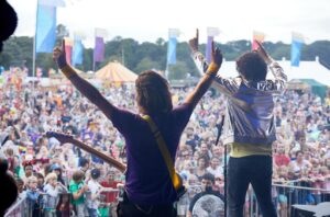 Two men on a stage at the Gloworm festival facing the crowd with their arms in the air