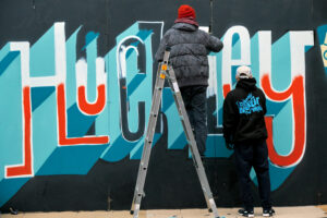 Two young people painting the word Hockley on a wall.