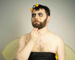Portrait of a man dressed in a bee costume with eye makeup running down his face.