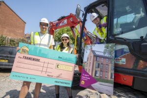 DHP Family Joseph Patten, Anwyn Williams and George Akins holding a novelty cheque next to a mobile digger