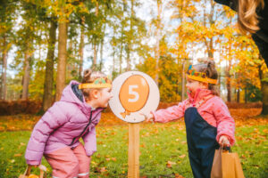 Two young girls stood by a sign in the forest with an easter egg pained on it with the number 5.