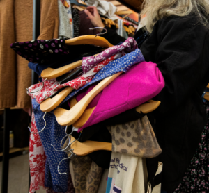 The image shows a lady holding a pile of clothes over her arm and browsing those on the racks.
