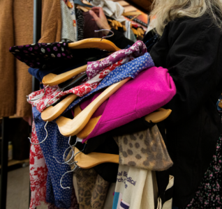 The image shows a lady holding a pile of clothes over her arm and browsing those on the racks.